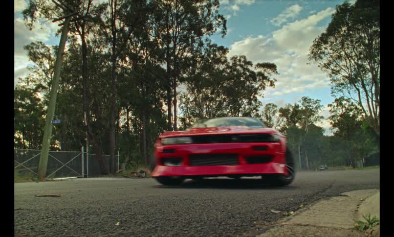 A red sports car drifts on a street surrounded by tall trees