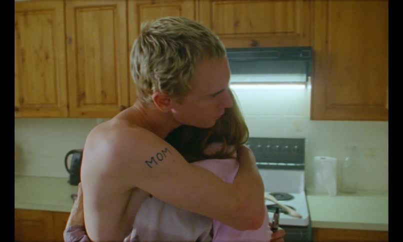 A man hugs a woman in the kitchen kisses her on the head and gently rubs her back with his hand