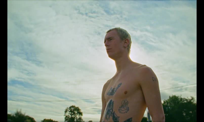 Shirtless man with tattoo on his body in an outdoor environment expelling smoke from his mouth