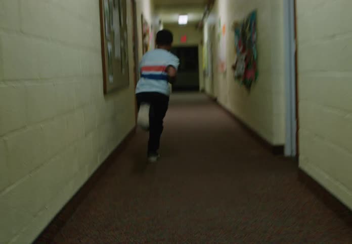 A young boy runs down a hallway lined with art and bulletin boards