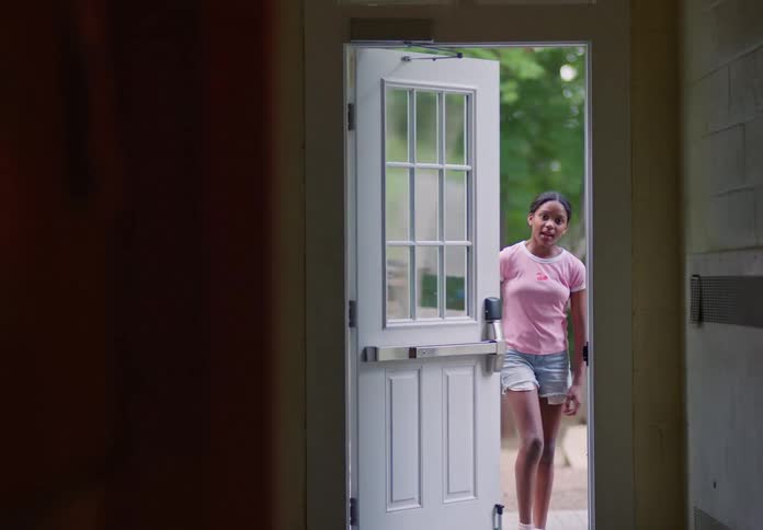 A girl walks through an open door into a house from outside