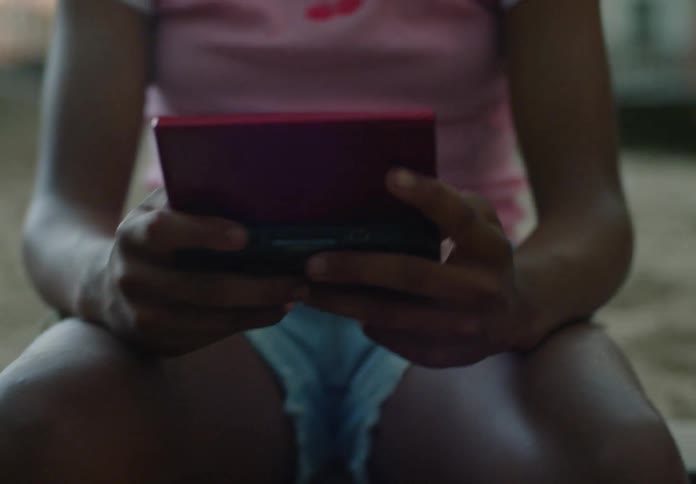 A teenage girl holds a handheld gaming device while playing outdoors