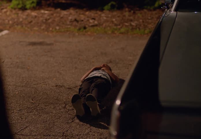 A girl looks worried when she finds a boy laying on the ground of the parking lot