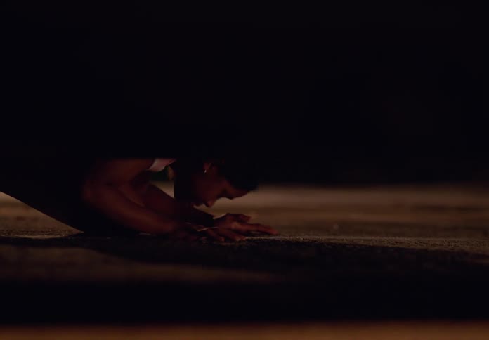 A teenage girl wearing white sneakers bends over to look under a car in search of something