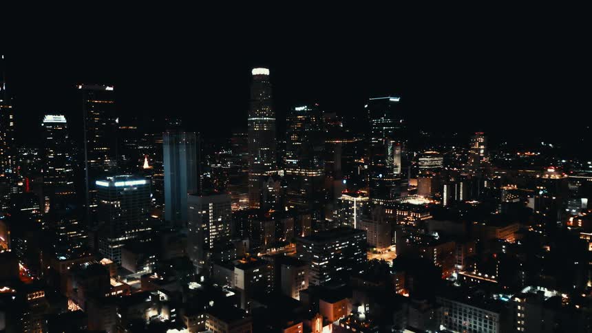 A sprawling city glows beneath a night sky with skyscrapers and lights stretching toward distant hills