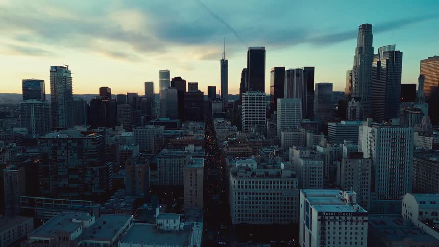 A wide angle view of downtown los angeles captures silhouetted skyscrapers against a golden orange sunset sky streaked with clouds