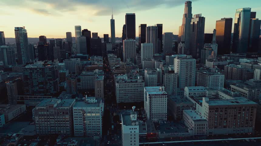 A wide angle view of downtown los angeles captures silhouetted skyscrapers against a golden orange sunset sky streaked with clouds
