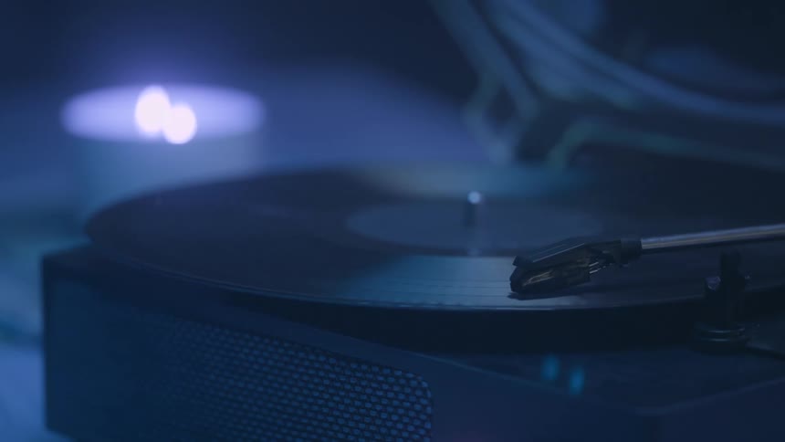 A closeup shot captures a vinyl record spinning on a turntable in a dimly lit room a soft blue light illuminates the scene highlighting the record and the stylus as it rests in the grooves