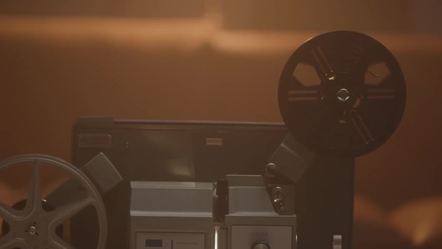 A vintage film projector with two reels is illuminated by warm ambient light