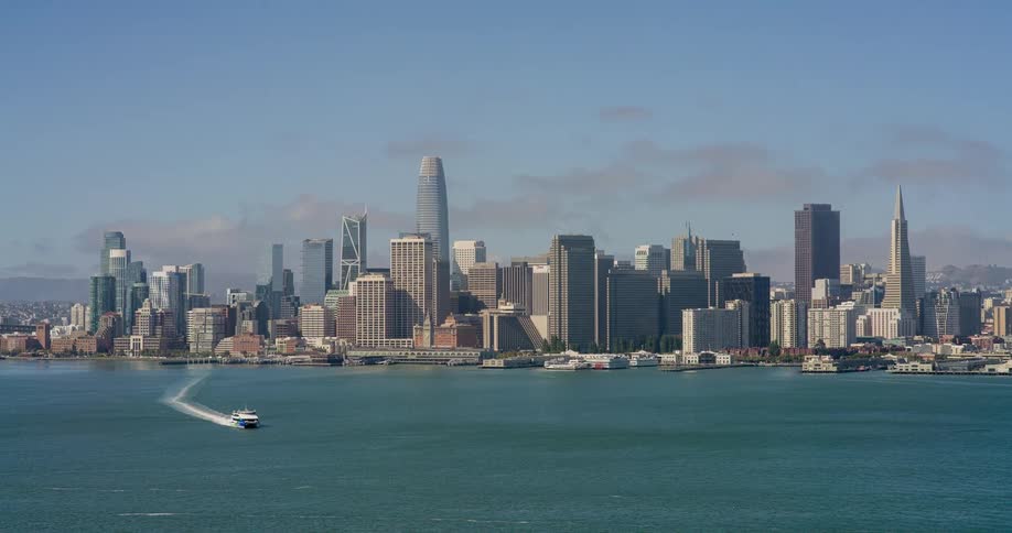 A city skyline along the shoreline with a boat passing through the ocean water at midday