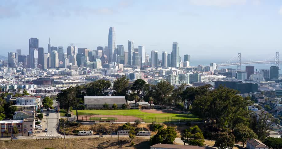 Baseball field surrounded by trees in the foreground with downtown san francisco and the bay bridge in the background