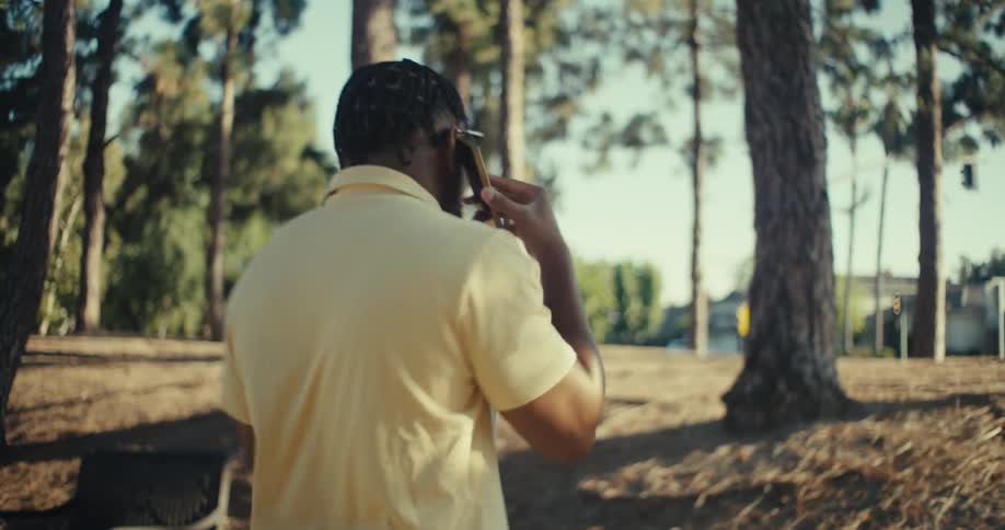 Young black man reacts happily while making a phone call as he walks through a park outdoors during daytime