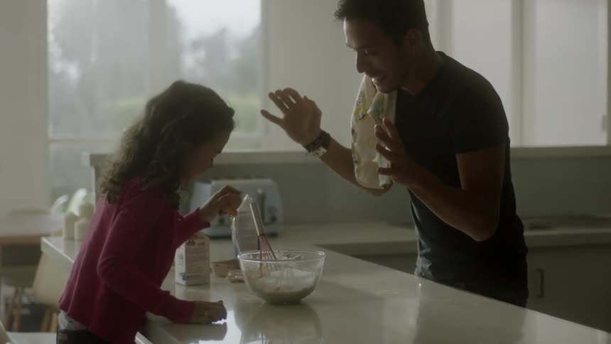 A man and young girl cook together in a kitchen