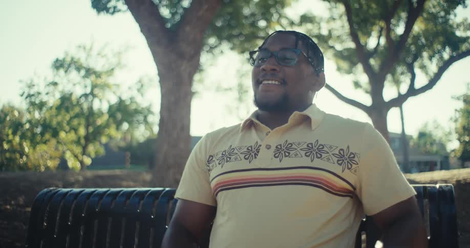 A happy man sits relaxed on a park bench using his phone