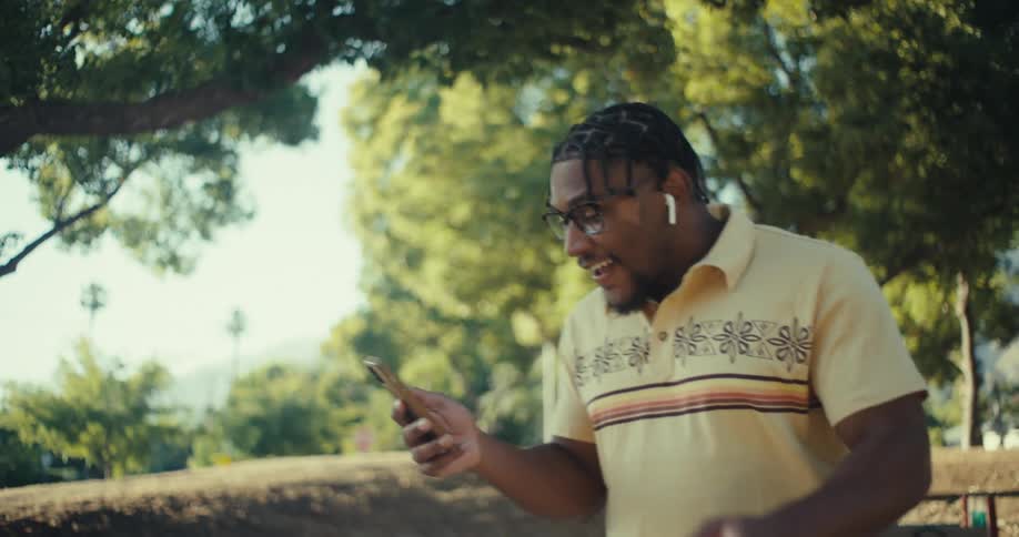 A cheerful man walks through a park while enjoying a video call