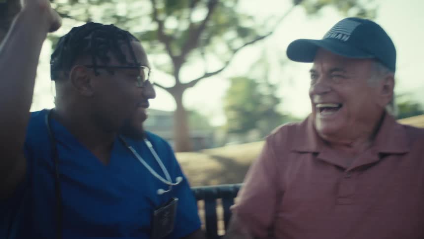 Young black doctor celebrates with an elderly man while sitting on a chair outdoors during daytime