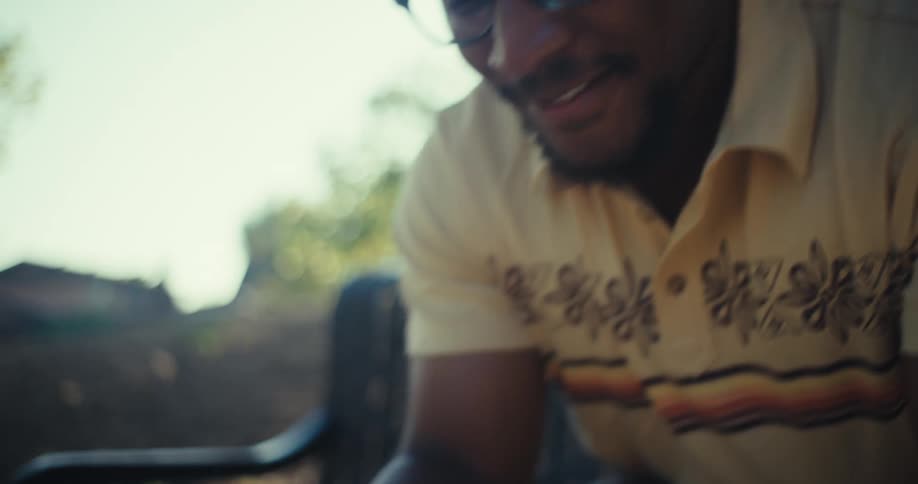 Close up of a young black man smiling as he uses a mobile phone while sitting outdoors during daytime