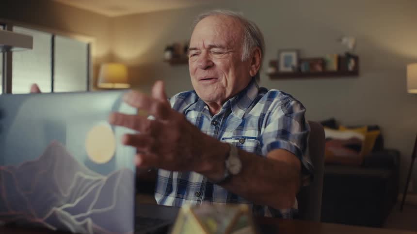 Elderly man celebrates after a call while sitting at a table in a living room during daytime