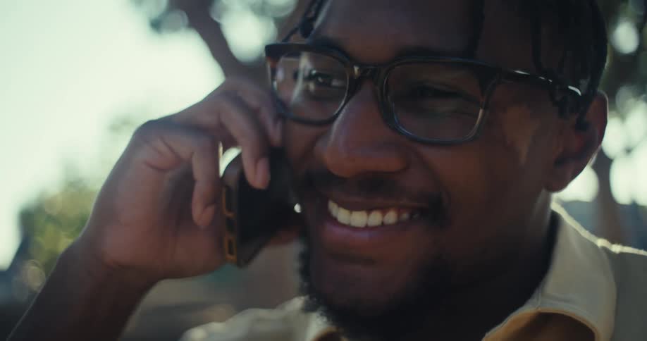 A man smiles while talking on the phone outdoors