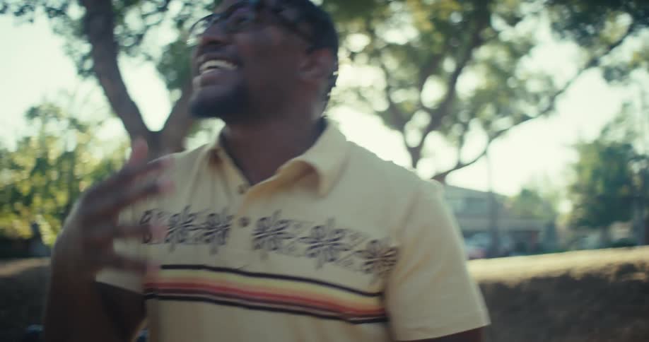 A man is walking outside talking on a cell phone and raising his arms in happiness
