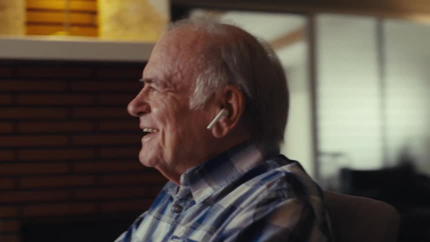 Elderly man with earbuds sitting in front of a laptop