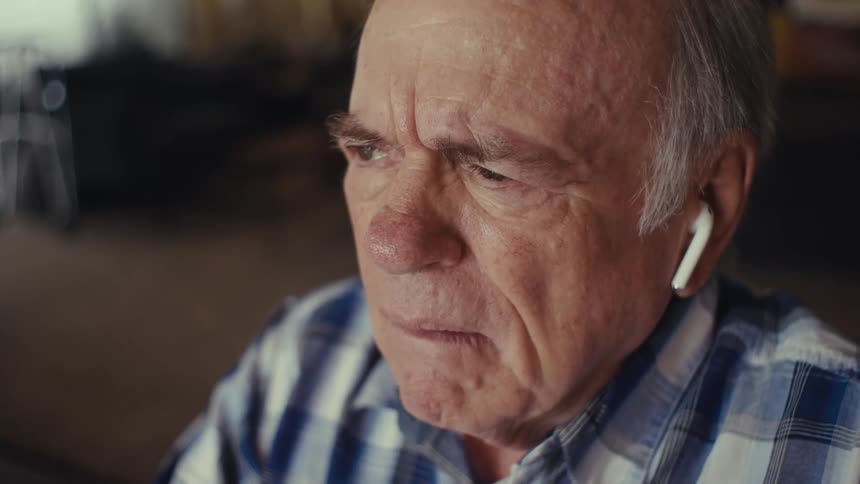 Close up portrait of an elderly man reacting emotionally on a call while sitting in a living room during daytime