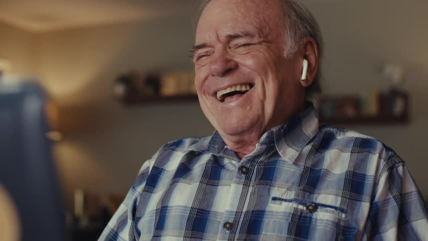 Elderly man laughs joyfully during a video call on a laptop