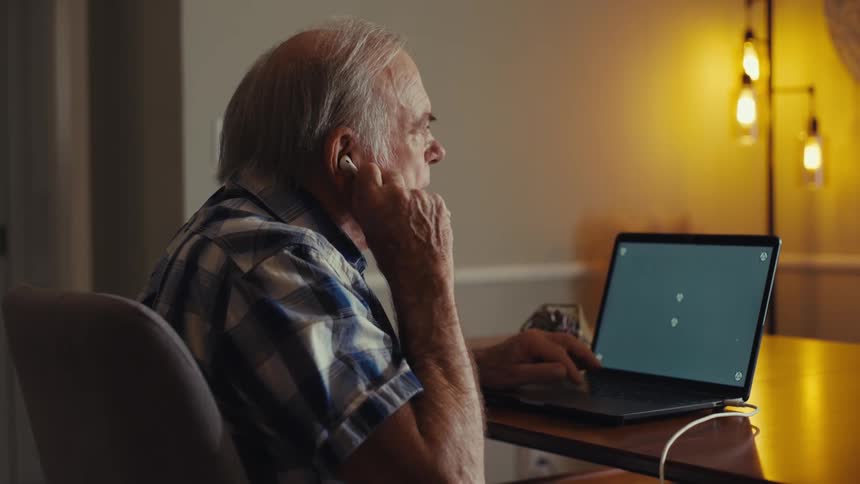 Elderly man sitting in front of a laptop looking thoughtful