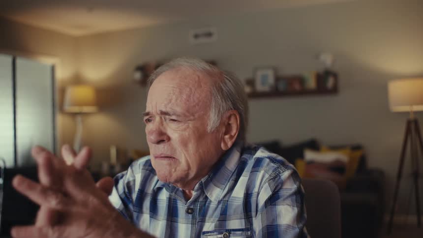 Elderly man folding his hands thoughtfully while sitting in a living room