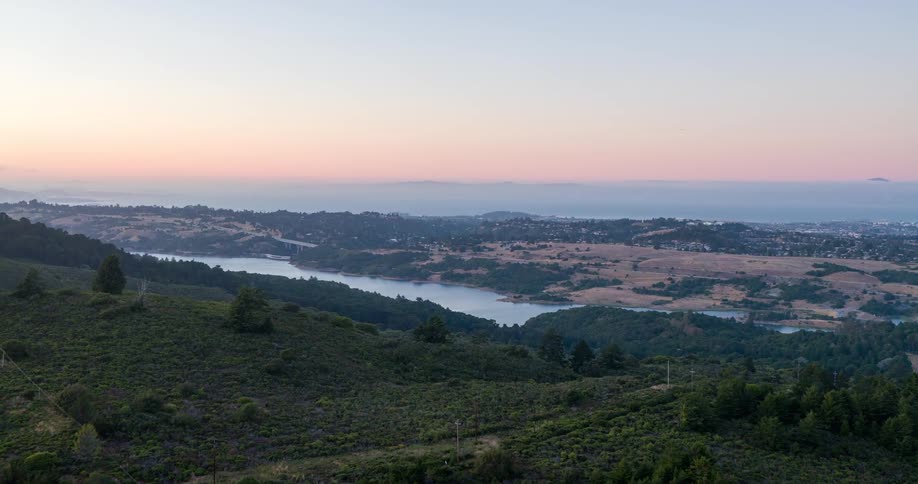 A peaceful landscape of rolling hills and a wide river at sunset