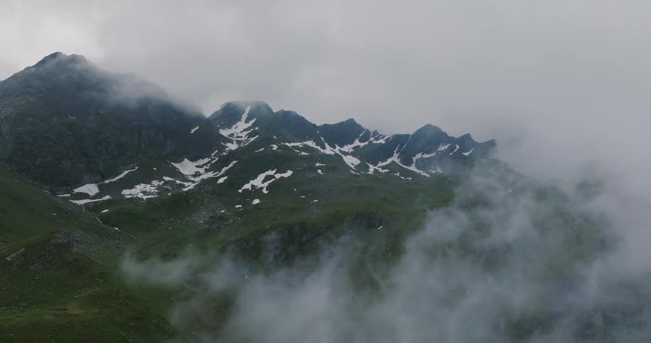 Fog drifts through a mountain valley with patches of snow under a cloudy sky