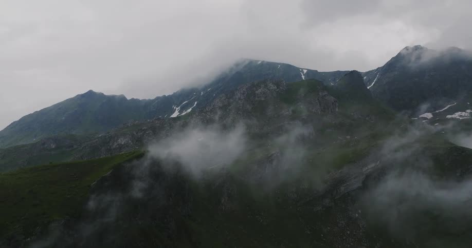 Panorama of greenish mountains with snow on a cloudy day