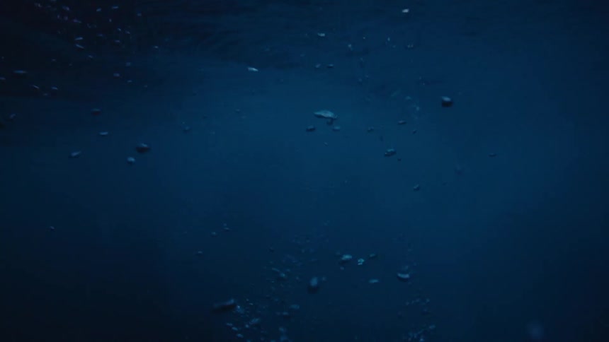 From underwater bubbles rise to the surface revealing a tropical island at sunset above the water