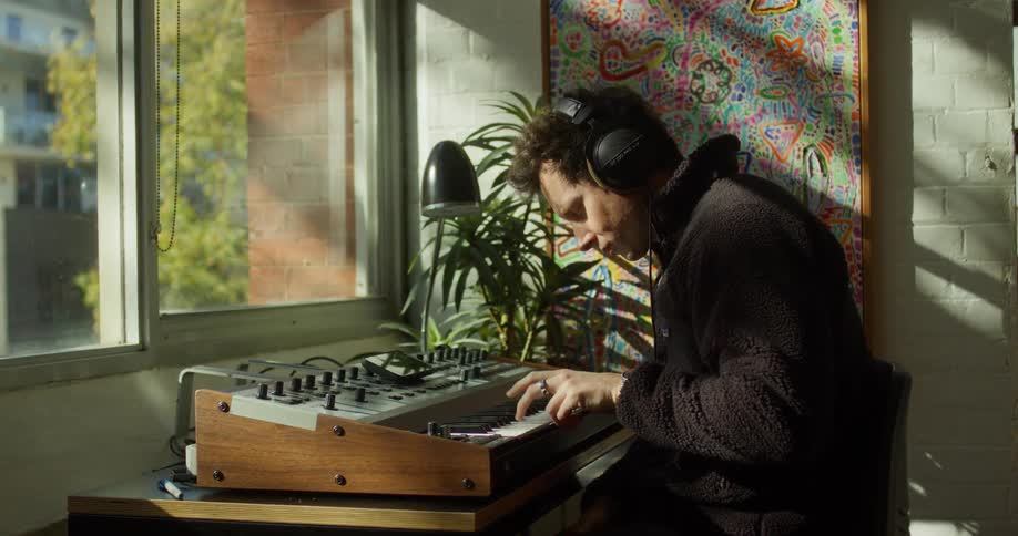 Young man makes music with a keyboard and audio equipment while sitting in a room during daytime