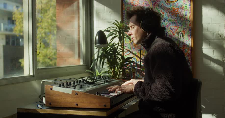 A young man plays a keyboard while sitting at a table in a room during daytime
