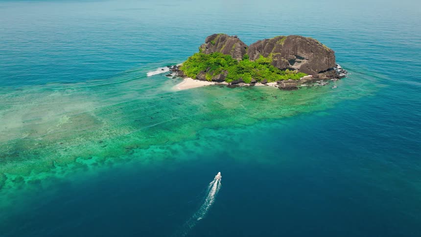 A rocky greencovered island sits in vivid turquoise water as a boat speeds away leaving a foamy trail behind