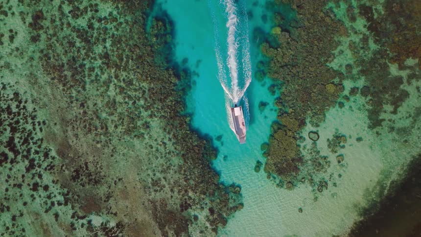 A small boat cruises through a vivid turquoise lagoon surrounded by scattered coral formations beneath a clear sky