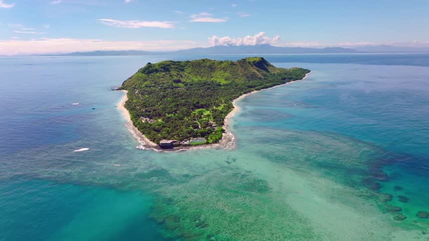 A lush green island with coral reefs and clear blue waters stretches into the ocean under a bright sunny sky