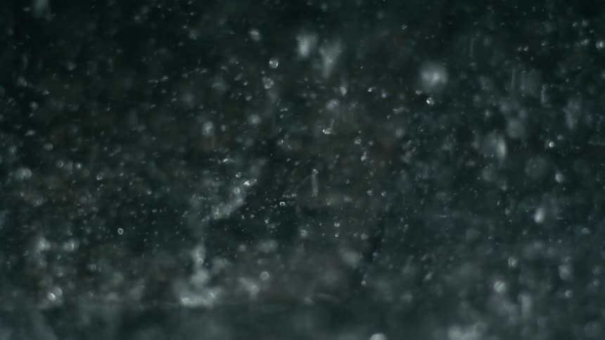 A close up view of heavy rain falling against a dark background with individual raindrops clearly visible as they streak downward in various sizes and shapes