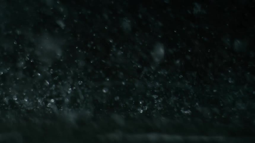 Countless raindrops splash against the ground in a dark environment