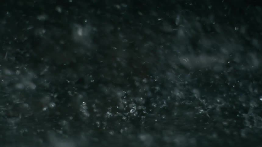 An extreme closeup of water droplets splashing and falling against a dark background creating a dynamic and textured visual effect the constant movement of the water creates a mesmerizing abstract pattern