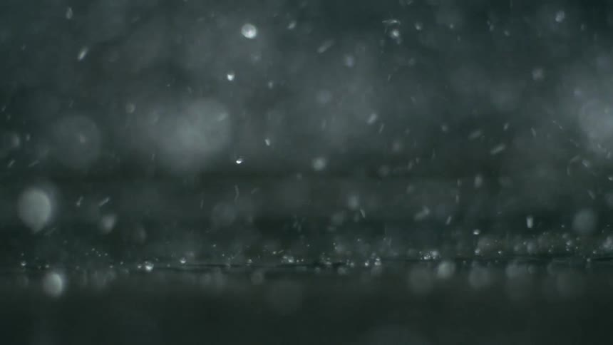 Close up of water droplets falling on a dark surface