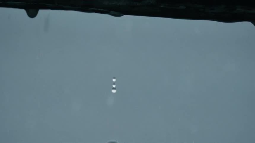 Close up of water droplets falling from a roof in the rain set against a stormy gray blue blur