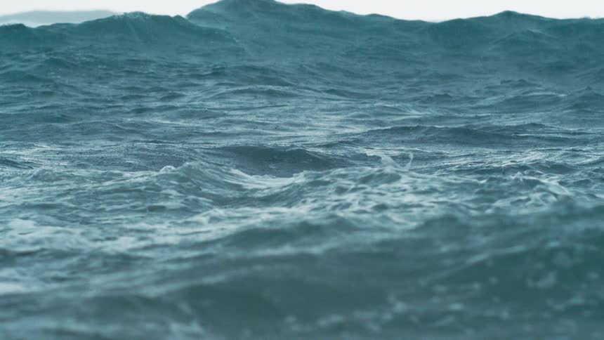Powerful turquoise ocean waves with white foam crest and churn under a bright white sky