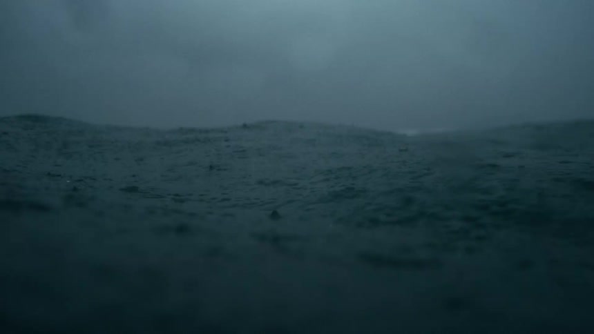 Dark turbulent ocean waves beneath a stormladen sky streaked with shifting gray clouds