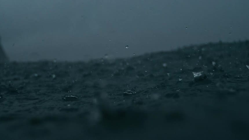 Rain falls over a fogshrouded ocean in the foreground with a distant shoreline and towering cliff partially obscured in the mist