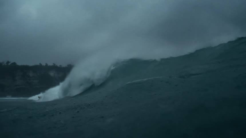 A person surfs a large wave under dark cloudy skies