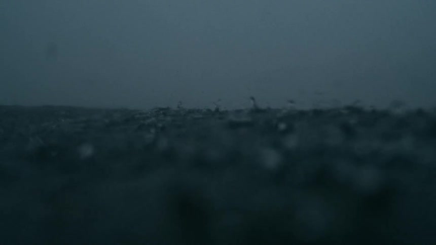 A dark stormy sea with choppy waves and heavy rainfall the horizon is barely visible through the thick grey mist and rain creating a bleak and intense atmosphere