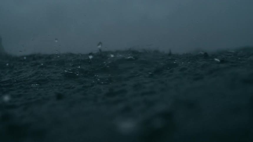 Dark choppy ocean waves churn and splash under rain