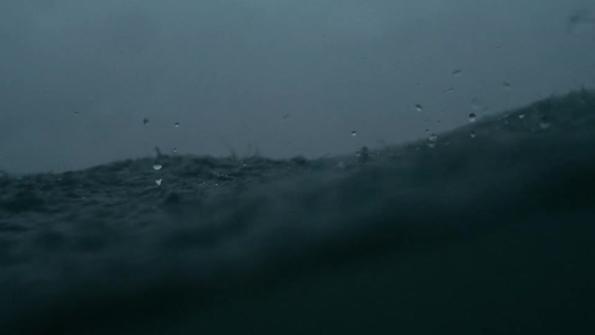 Heavy rain falling on a body of water creating ripples and splashes on the surface the background is a blurred dark horizon suggesting either a vast body of water or distant land obscured by the downpour